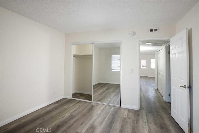 unfurnished bedroom with a closet, visible vents, a textured ceiling, and wood finished floors