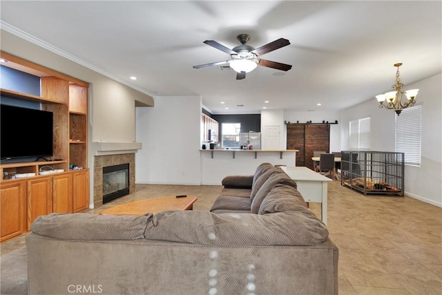 living area with visible vents, a tiled fireplace, a barn door, ornamental molding, and ceiling fan