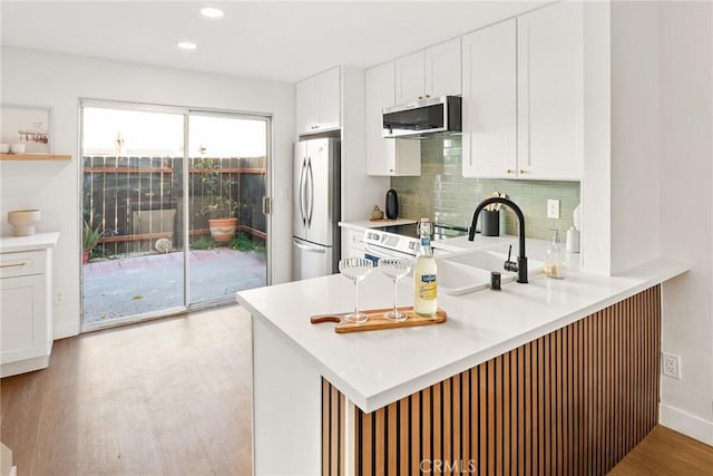 kitchen with white cabinets, appliances with stainless steel finishes, a peninsula, light wood-type flooring, and backsplash