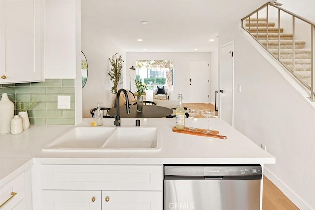 kitchen with a peninsula, a sink, white cabinetry, decorative backsplash, and dishwasher