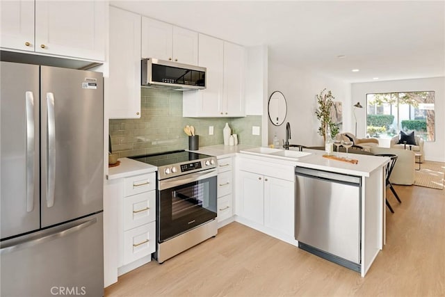 kitchen with open floor plan, stainless steel appliances, light wood-type flooring, and a peninsula