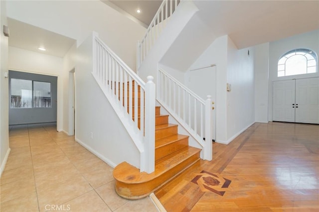 foyer entrance with stairs, light tile patterned flooring, a towering ceiling, and baseboards