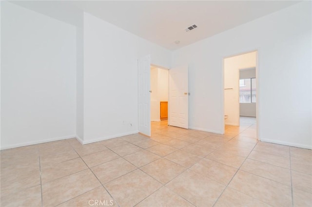 empty room featuring light tile patterned flooring, visible vents, and baseboards