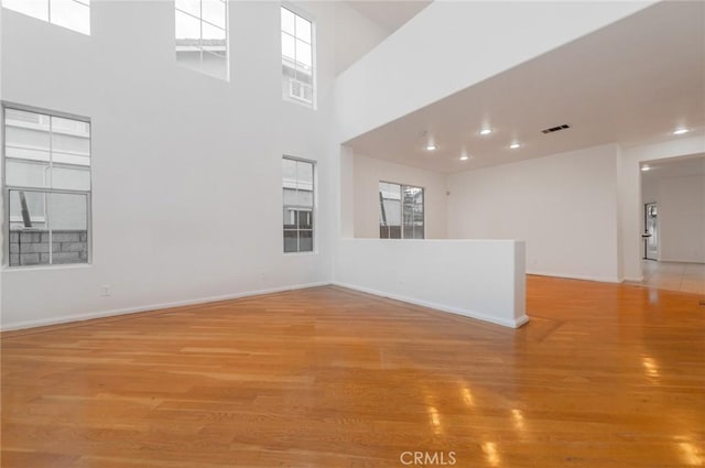 unfurnished room featuring baseboards, visible vents, light wood-style flooring, and a high ceiling