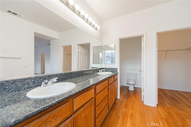 bathroom with double vanity, wood finished floors, a sink, and toilet