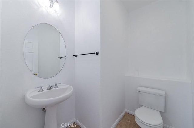 half bath featuring tile patterned flooring, toilet, and baseboards