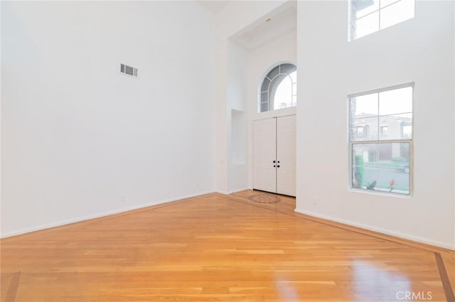 foyer with light wood-style flooring, visible vents, a towering ceiling, and baseboards