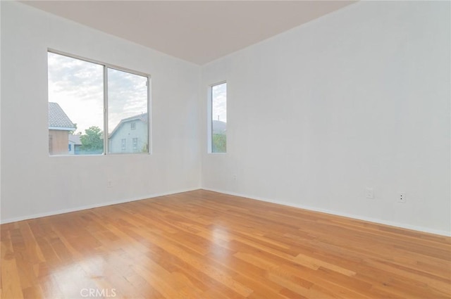 empty room featuring light wood-style floors, plenty of natural light, and baseboards