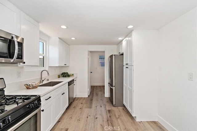 kitchen with appliances with stainless steel finishes, light wood-type flooring, a sink, and white cabinetry