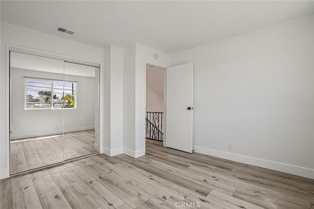 unfurnished bedroom with a closet, wood finished floors, visible vents, and baseboards