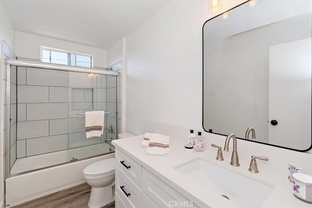 bathroom with toilet, bath / shower combo with glass door, wood finished floors, and vanity