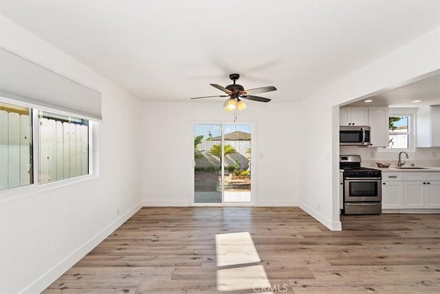 interior space with light wood finished floors, a ceiling fan, baseboards, and a sink