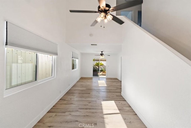 corridor featuring light wood-style floors, a high ceiling, visible vents, and baseboards