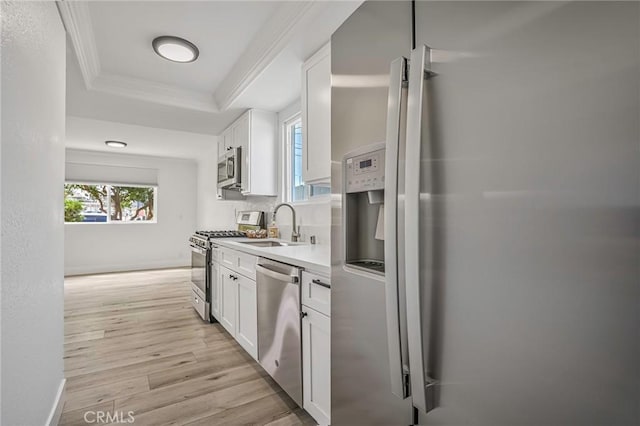 kitchen with appliances with stainless steel finishes, a tray ceiling, light wood-type flooring, white cabinetry, and a sink