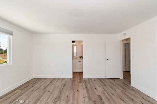 unfurnished bedroom featuring light wood-style floors, connected bathroom, and baseboards