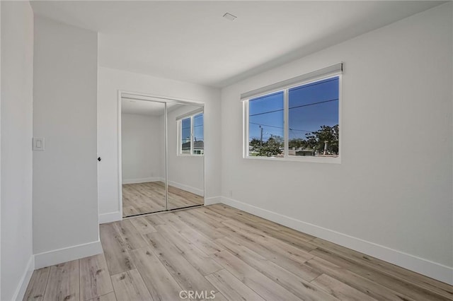 unfurnished bedroom featuring a closet, baseboards, and light wood finished floors