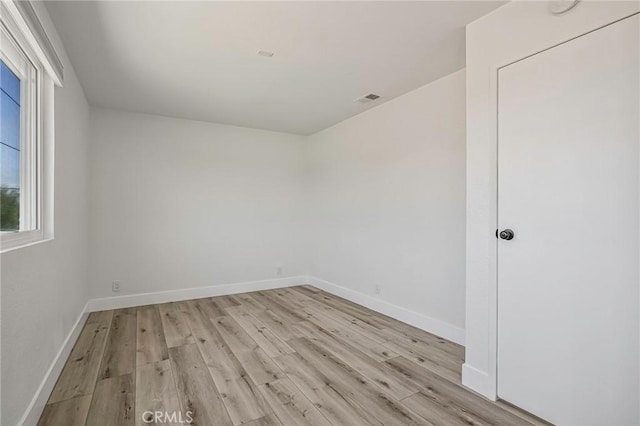 spare room with light wood finished floors, visible vents, and baseboards