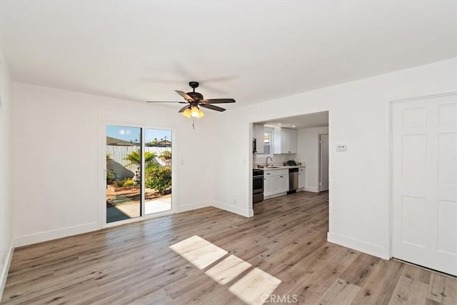 unfurnished living room featuring light wood-style floors, a sink, baseboards, and ceiling fan