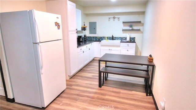 kitchen with white cabinets, light wood-style floors, freestanding refrigerator, and a sink