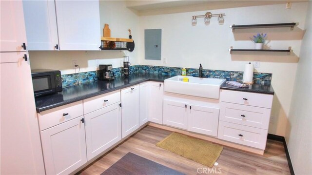 kitchen featuring electric panel, a sink, black microwave, and open shelves