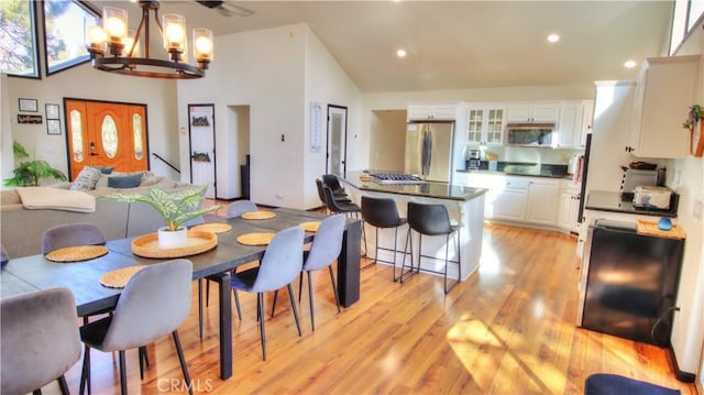 dining space with recessed lighting, high vaulted ceiling, a chandelier, and light wood finished floors