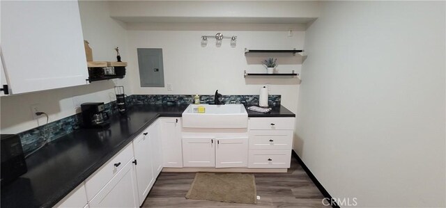 bathroom with wood finished floors, baseboards, electric panel, a sink, and backsplash