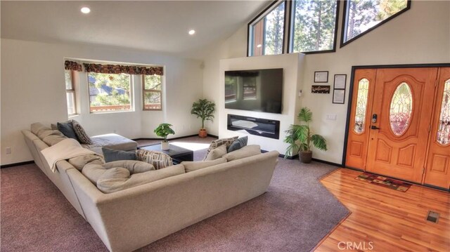 living area featuring wood finished floors, baseboards, high vaulted ceiling, recessed lighting, and a glass covered fireplace