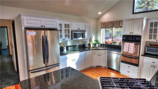 kitchen featuring glass insert cabinets, stainless steel appliances, a warming drawer, and vaulted ceiling