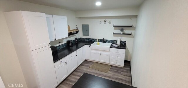 kitchen featuring a sink, dark countertops, wood finished floors, and white cabinetry