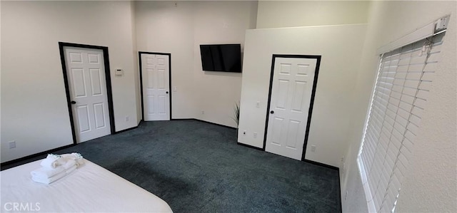 unfurnished bedroom featuring baseboards, dark colored carpet, and a towering ceiling