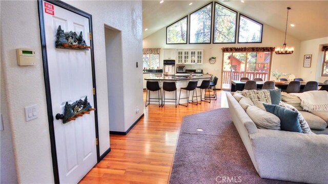 living room featuring a notable chandelier, light wood finished floors, and high vaulted ceiling