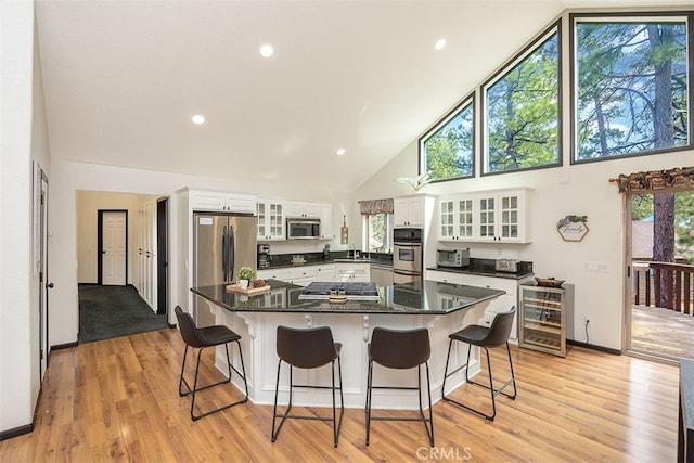 kitchen with appliances with stainless steel finishes, high vaulted ceiling, wine cooler, white cabinetry, and light wood-type flooring