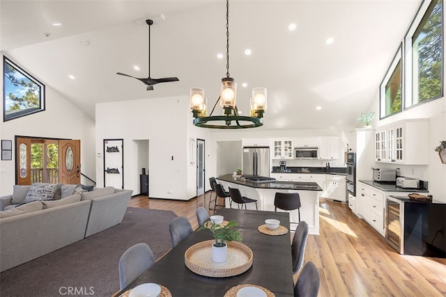 dining space featuring high vaulted ceiling, light wood finished floors, a chandelier, recessed lighting, and wine cooler