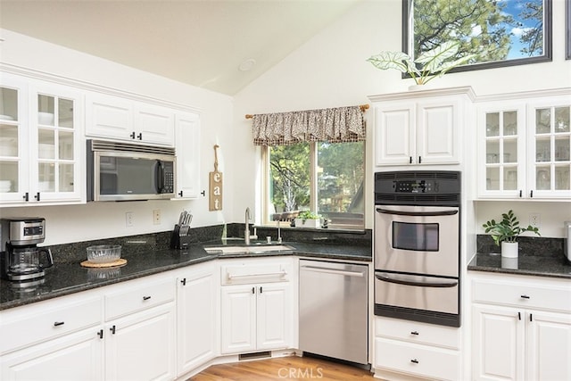 kitchen featuring stainless steel appliances, a sink, a warming drawer, white cabinetry, and dark stone countertops