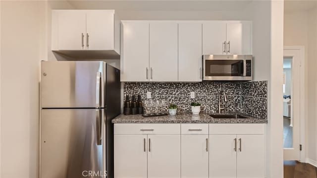 kitchen featuring stainless steel appliances, a sink, white cabinetry, and decorative backsplash