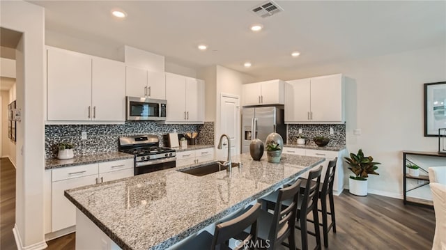 kitchen featuring visible vents, appliances with stainless steel finishes, a kitchen island with sink, a sink, and a kitchen bar