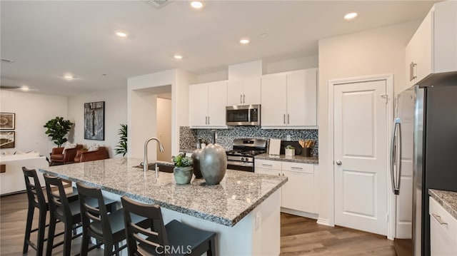 kitchen featuring stainless steel appliances, a breakfast bar, a sink, tasteful backsplash, and dark wood finished floors