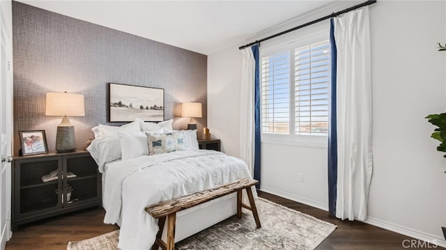 bedroom featuring an accent wall, dark wood-style flooring, and baseboards