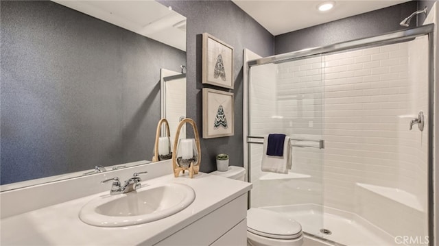 full bath featuring a textured wall, vanity, a shower stall, and toilet