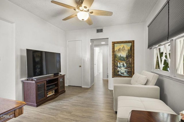 living room with a textured ceiling, visible vents, baseboards, ceiling fan, and wood finished floors
