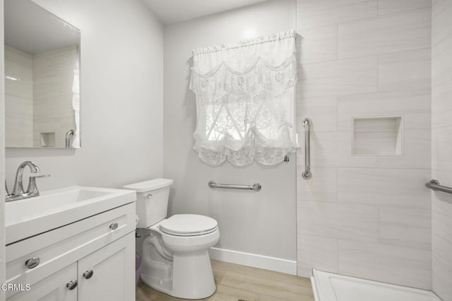 full bathroom with baseboards, toilet, wood finished floors, vanity, and tiled shower