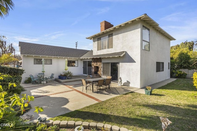 rear view of house featuring a lawn, a chimney, stucco siding, and a patio