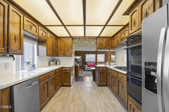 kitchen with light countertops, light wood-style flooring, appliances with stainless steel finishes, ventilation hood, and brown cabinetry