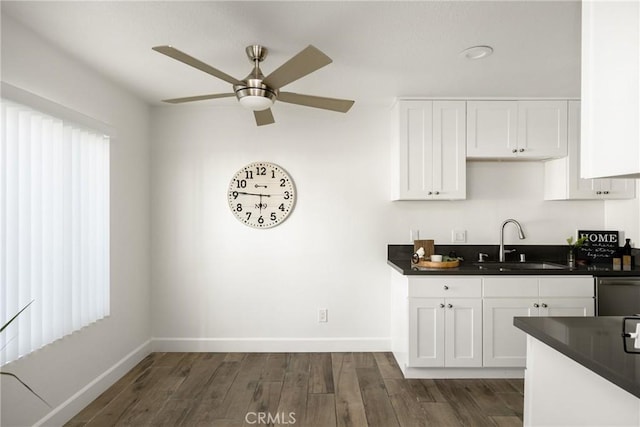 kitchen with ceiling fan, a sink, dark wood-type flooring, stainless steel dishwasher, and dark countertops