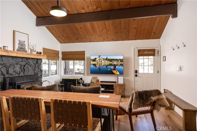 dining area featuring vaulted ceiling with beams, wood ceiling, wood finished floors, and a stone fireplace