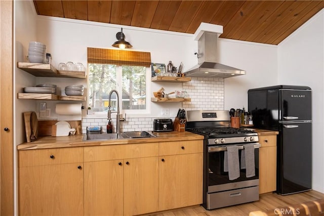 kitchen featuring freestanding refrigerator, stainless steel gas stove, wall chimney exhaust hood, and open shelves