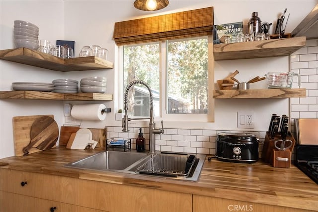 kitchen featuring tasteful backsplash, wooden counters, open shelves, and a sink