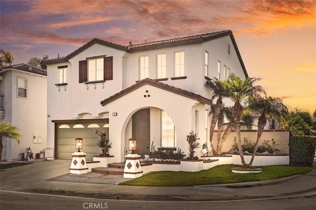 back of property at dusk with a garage, concrete driveway, a tiled roof, and stucco siding