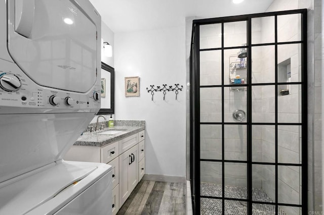 full bath featuring wood finished floors, stacked washer and clothes dryer, vanity, and tiled shower