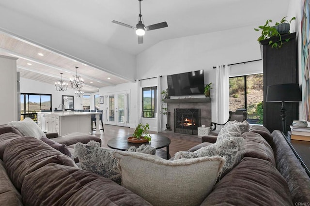 living room featuring vaulted ceiling, a warm lit fireplace, ceiling fan with notable chandelier, and a wealth of natural light